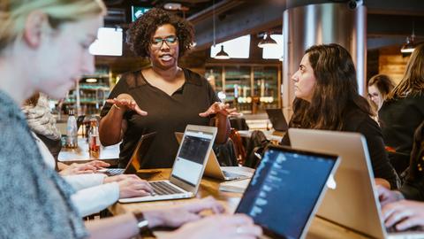 Woman speaking to conference table of students on laptops
