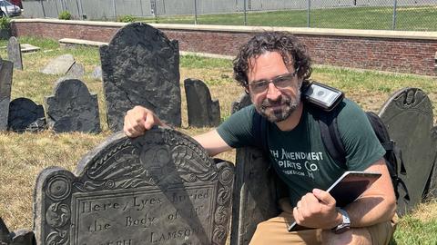 Jason Ur kneels next to the headstone of Joseph Lamson