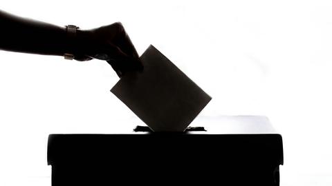 silhouette of a hand placing a ballot into a ballot box