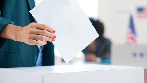 Close-up of a person about to drop a voting ballot into a ballot box at a polling place