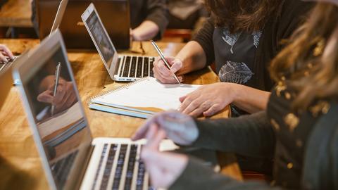 Close-up on students working at laptops and writing in a notebook