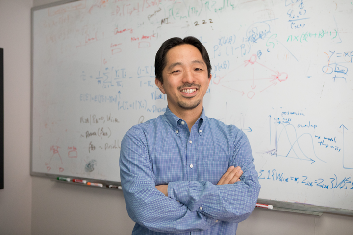 Kosuke Imai in front of a white board