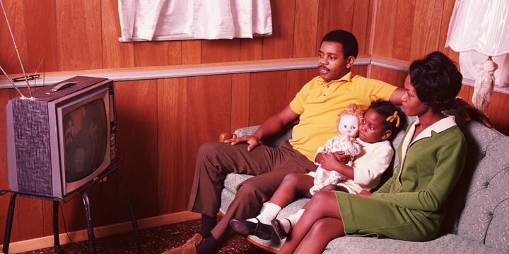 70s or 80s couple with small child on sofa watching TV