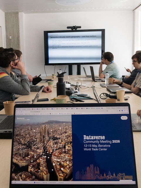 DCM 2026 attendees at a conference table, with a laptop in the foreground showing the event home page on its screen